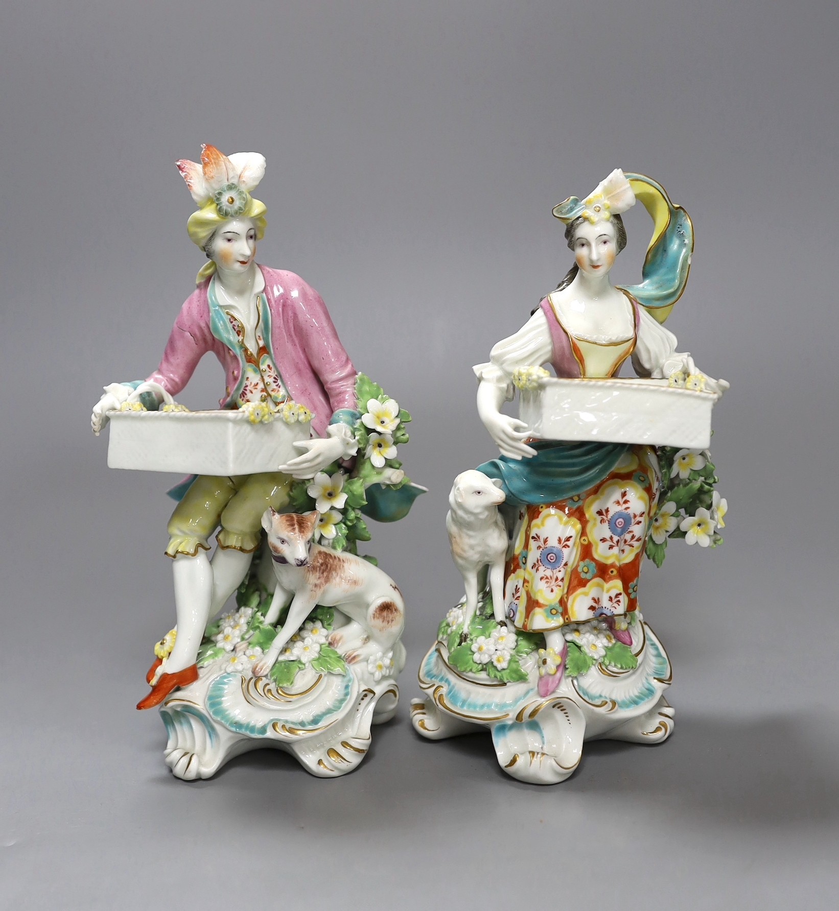 Two Derby sweetmeat figures, each seated and resting with an open rectangular basket on their knees, c.1760-65, patch marks, 20cm